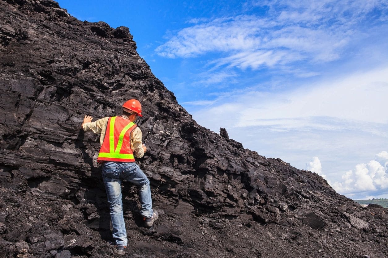 A man in an orange vest climbing up a pile of coal.